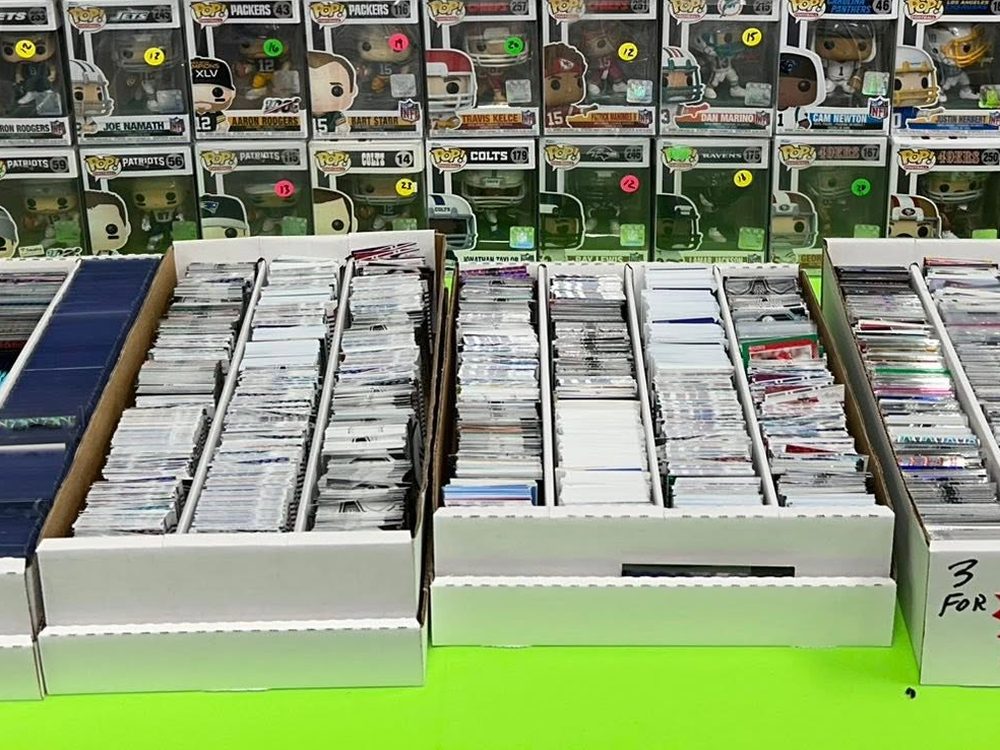 Long boxes of loose cards priced for digging, with Funko Pops behind them