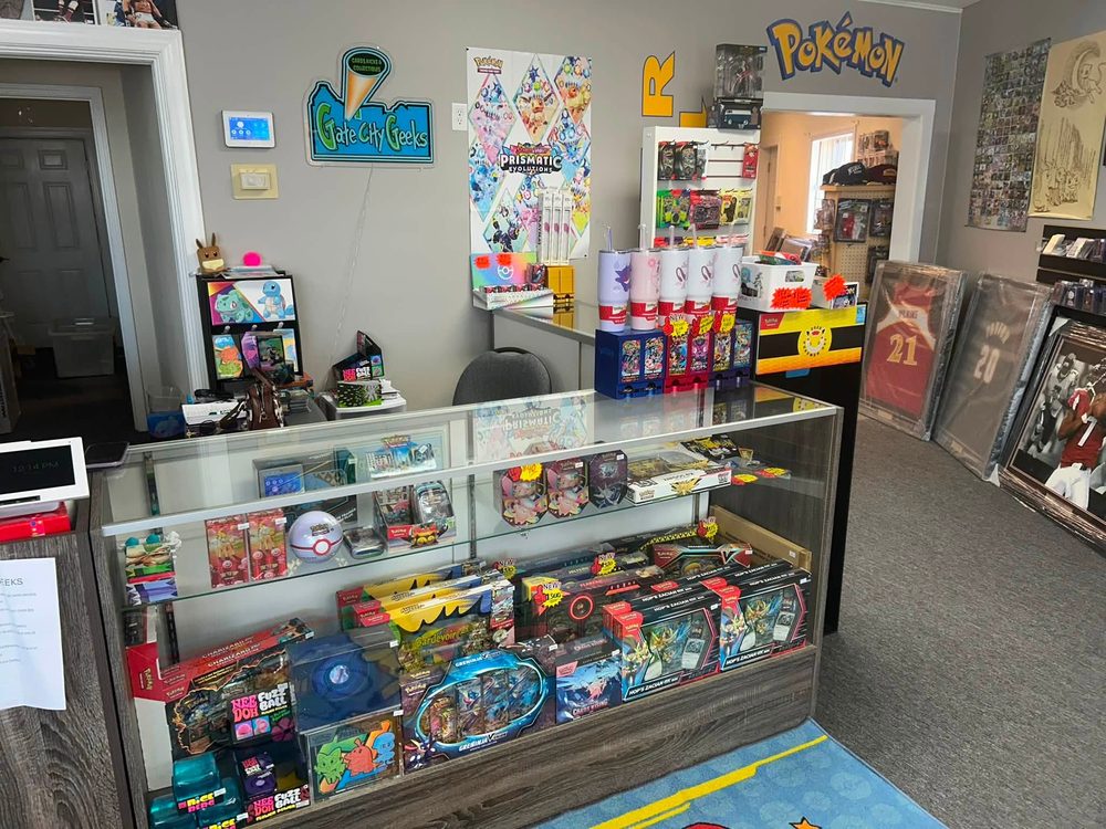 Pokemon counter with sealed tins, elite trainer boxes and the Gate City Geeks neon sign