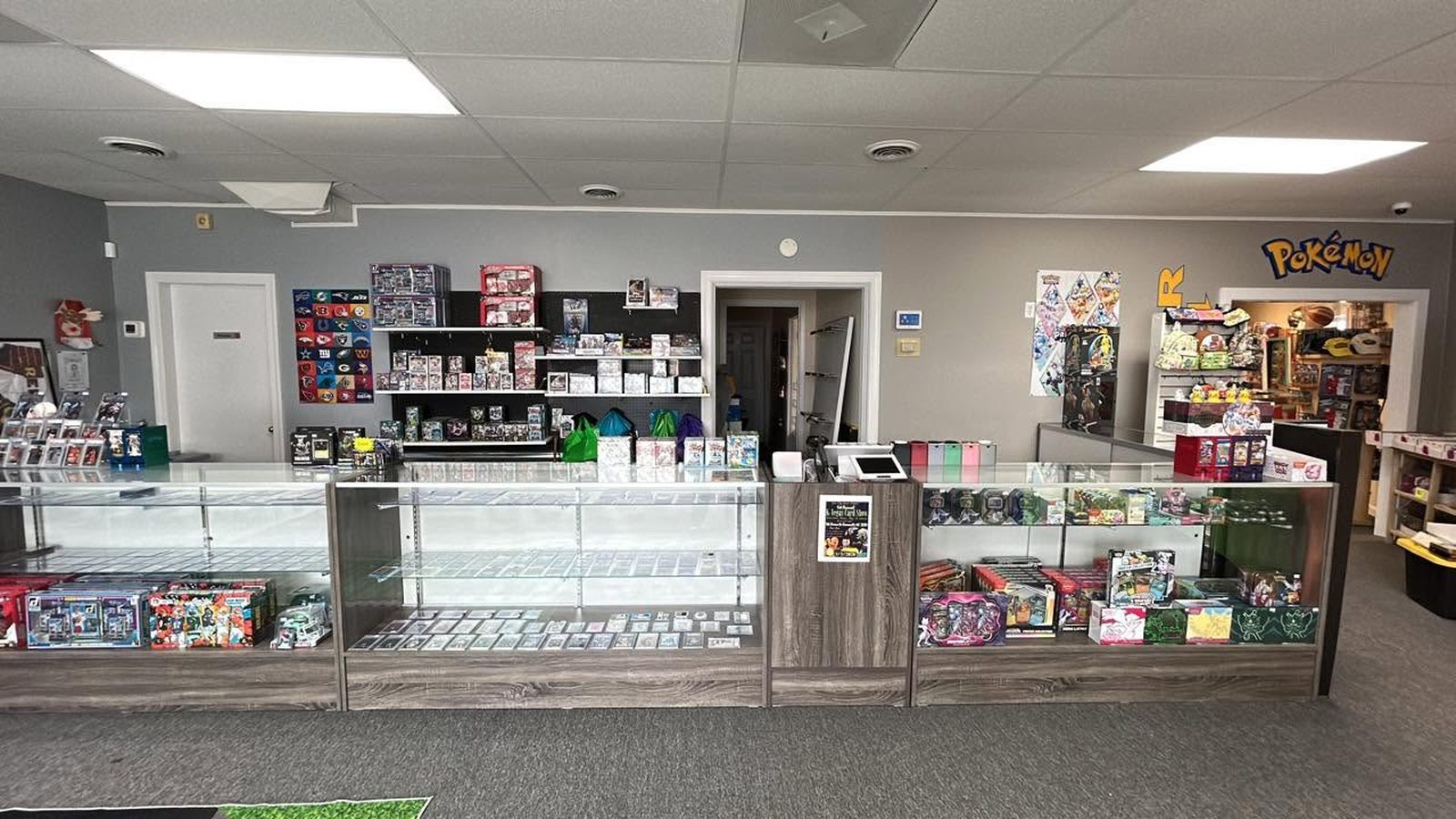 Inside Gate City Geeks: lit glass cases running the length of the shop with sealed product and singles